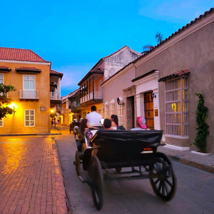 A romantic evening carriage ride through the narrow streets of Cartagena, Colombia, with historic colonial buildings illuminated under the soft glow of street lights.