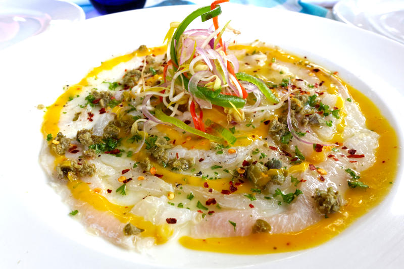 A beautifully plated ceviche dish topped with fresh herbs, thinly sliced onions, and colorful peppers, drizzled with citrus sauce.